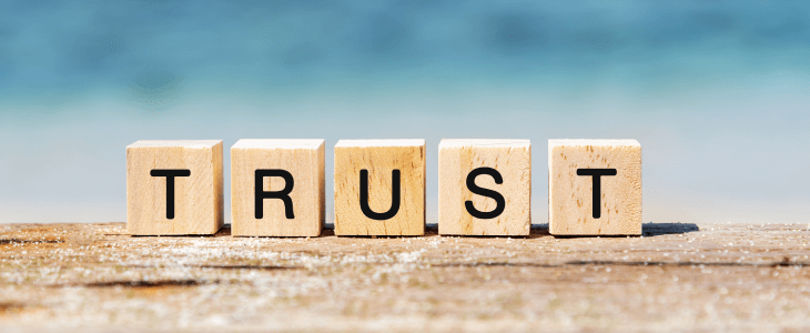 "TRUST" written on wooden blocks in front of the shore of a beach to represent Offshore Trusts.